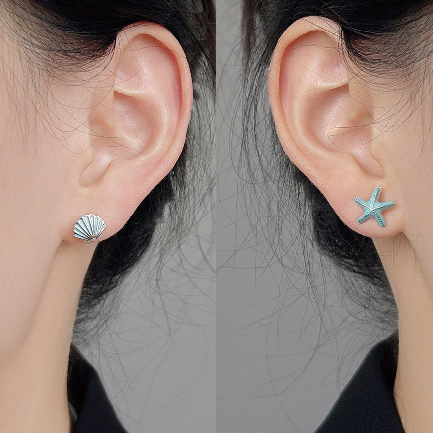A woman wearing the asymmetrical silver-plated starfish and seashell stud earrings.