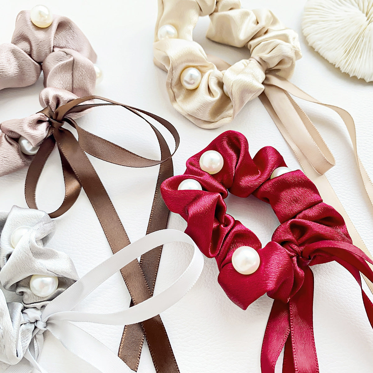 A collection of colorful silk hair scrunchies with pearl and ribbon details
