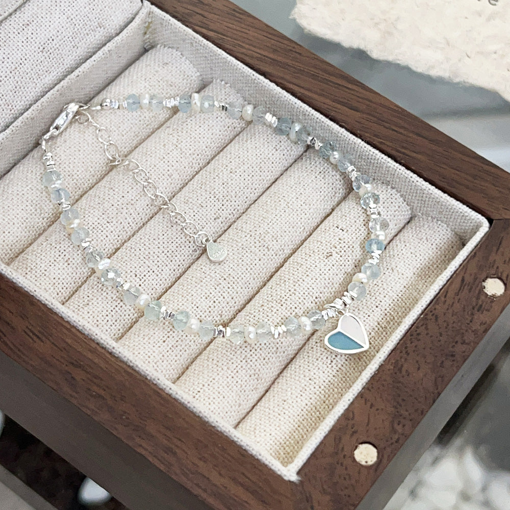 A sterling silver heart charm bracelet elegantly displayed in a wooden jewelry box