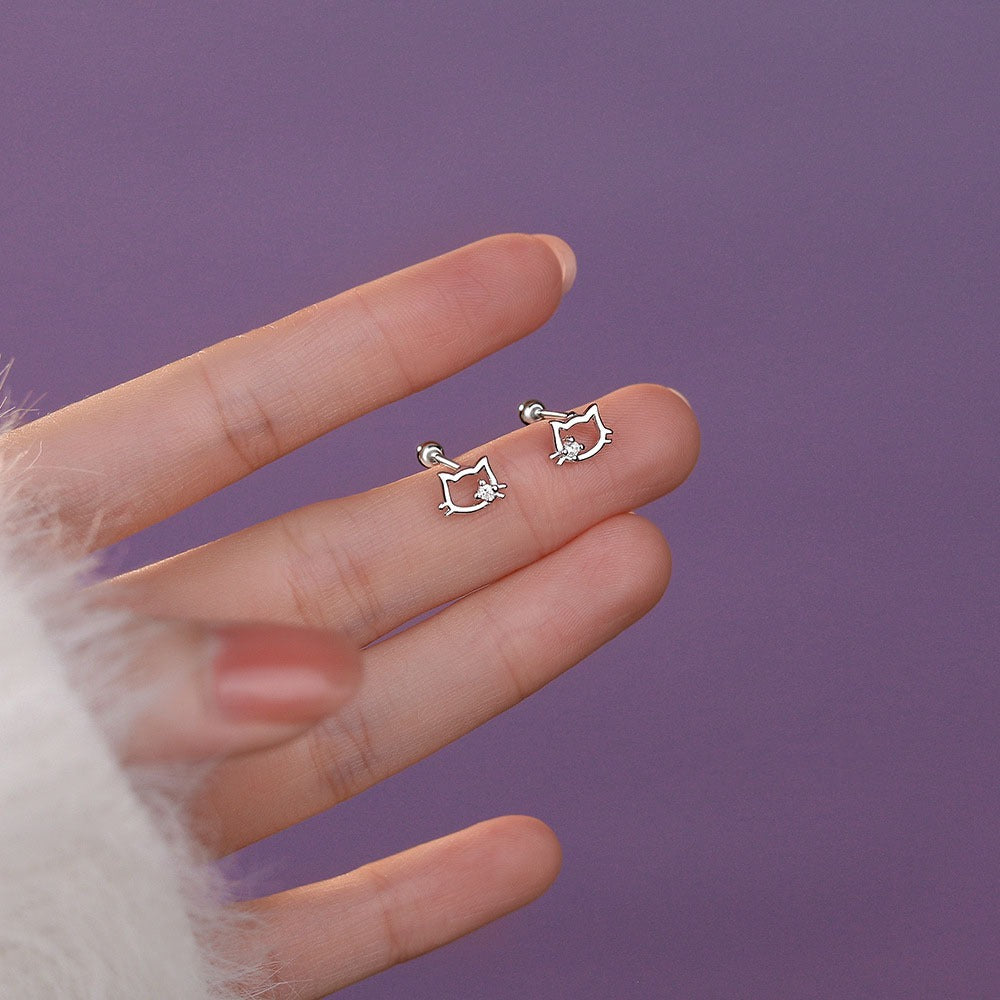 A pair of silver cat ear stud earrings with cubic zirconia displayed on a soft pink background.