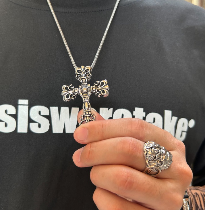 A silver cross necklace displayed alongside a matching textured ring to showcase the collection.