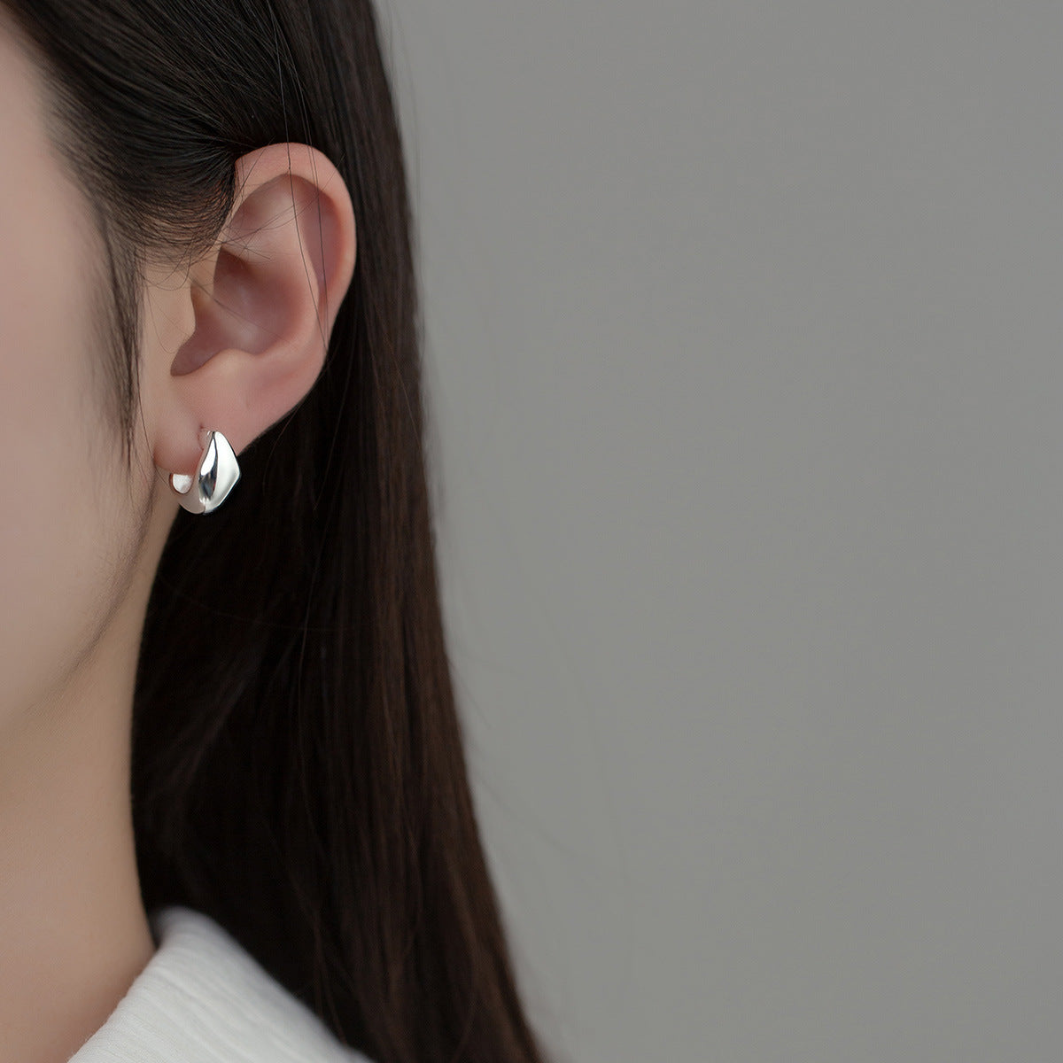 Detailed close-up of a silver irregular geometric huggie hoop earring
