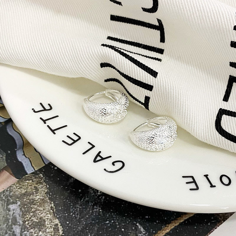 A pair of 925 sterling silver textured hoop earrings on a decorative plate