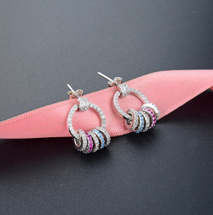 A pair of minimalist 925 sterling silver drop earrings with colorful zircon stones on a white background.