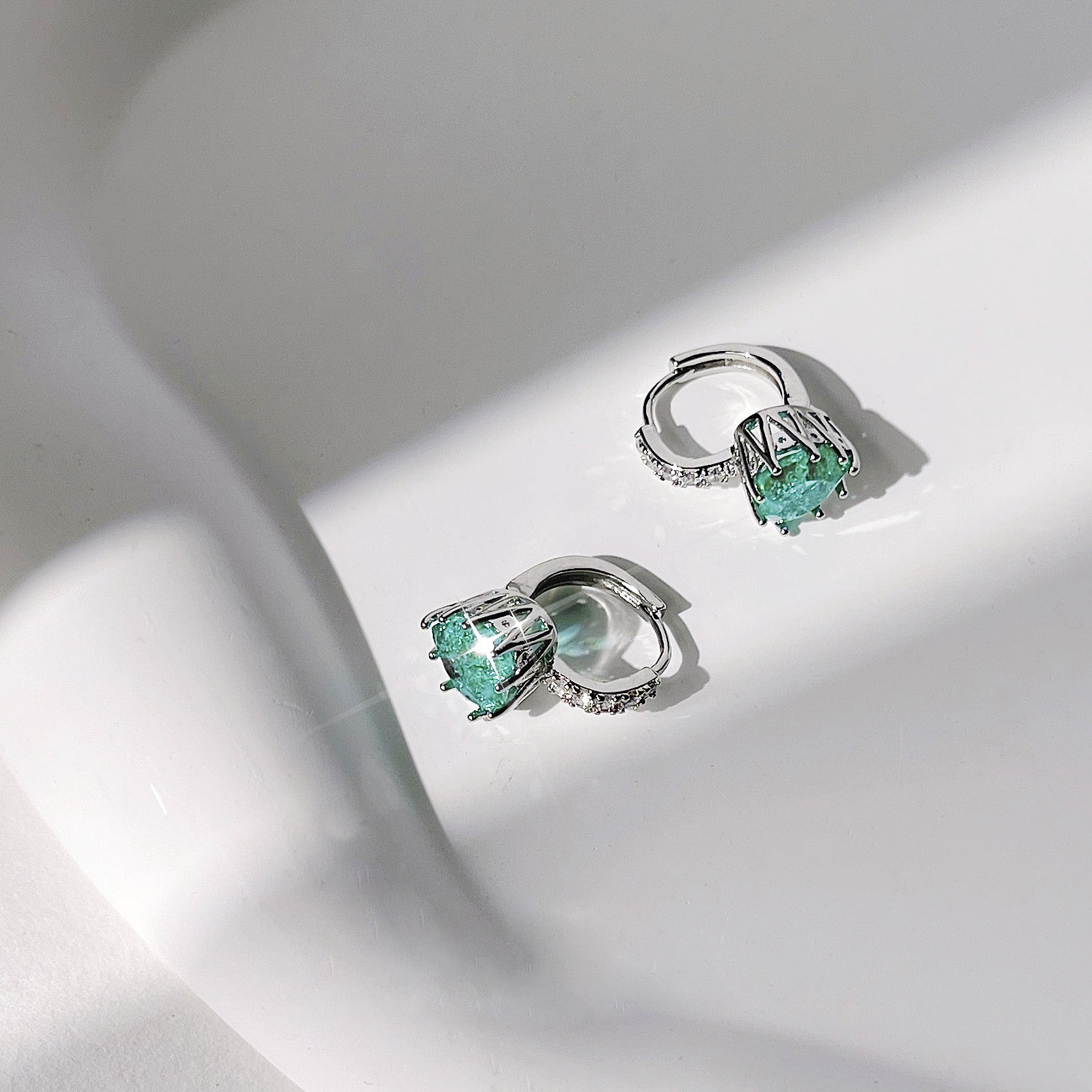 A pair of silver earrings with green gemstones and smaller white gemstones, showcasing the quality craftsmanship.