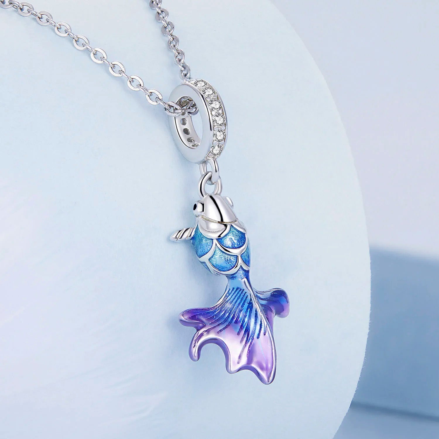 A silver fish-shaped pendant with a blue-to-purple gradient and clear stones, displayed on a silver chain.