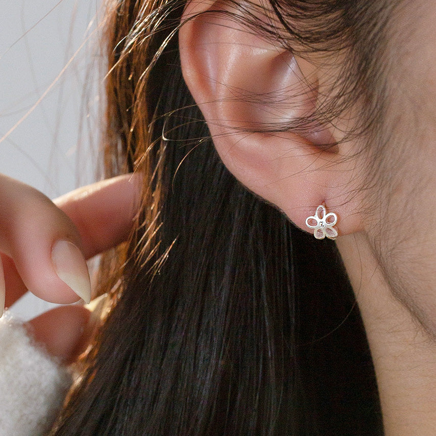 A close-up of a woman wearing the mini 925 sterling silver flower huggie earring.