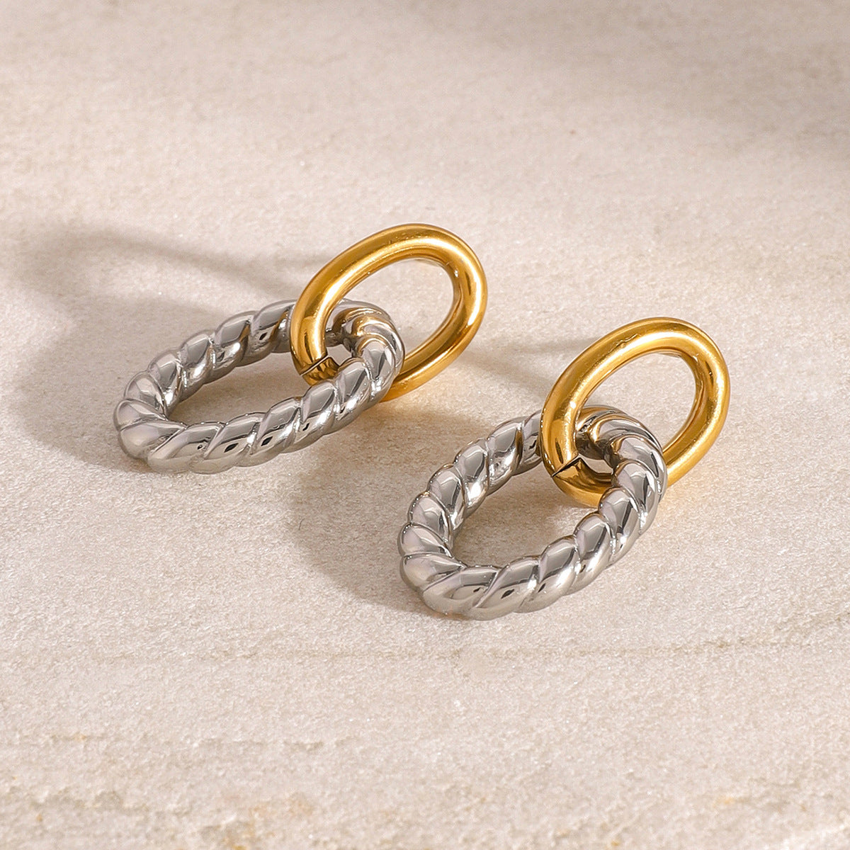 A detailed close-up of the two-tone oval twist earrings, showing the interplay of gold and silver stainless steel.