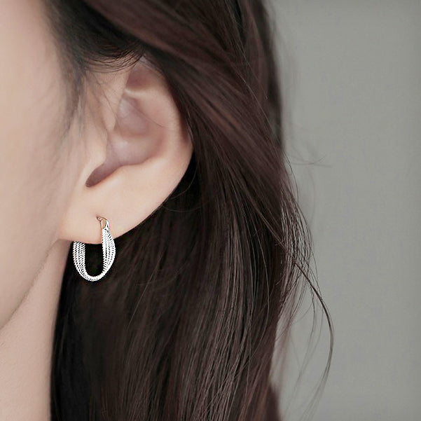 A woman wearing the twisted sterling silver huggie hoop earring.