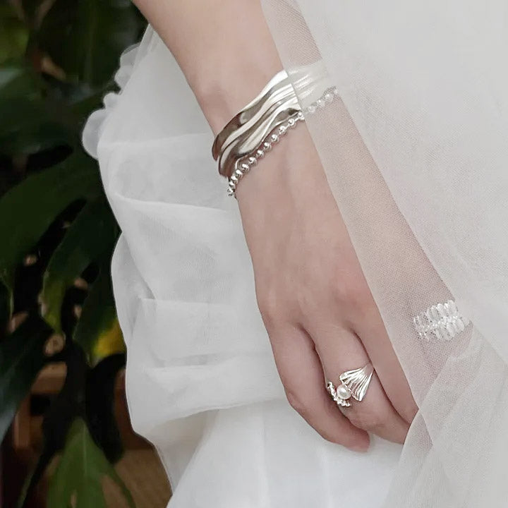 A model's hand adorned with multiple sterling silver shell and pearl rings from the set.