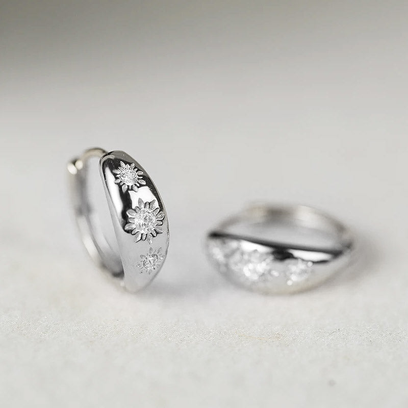 A pair of silver CZ starburst huggie hoop earrings with intricate floral designs.