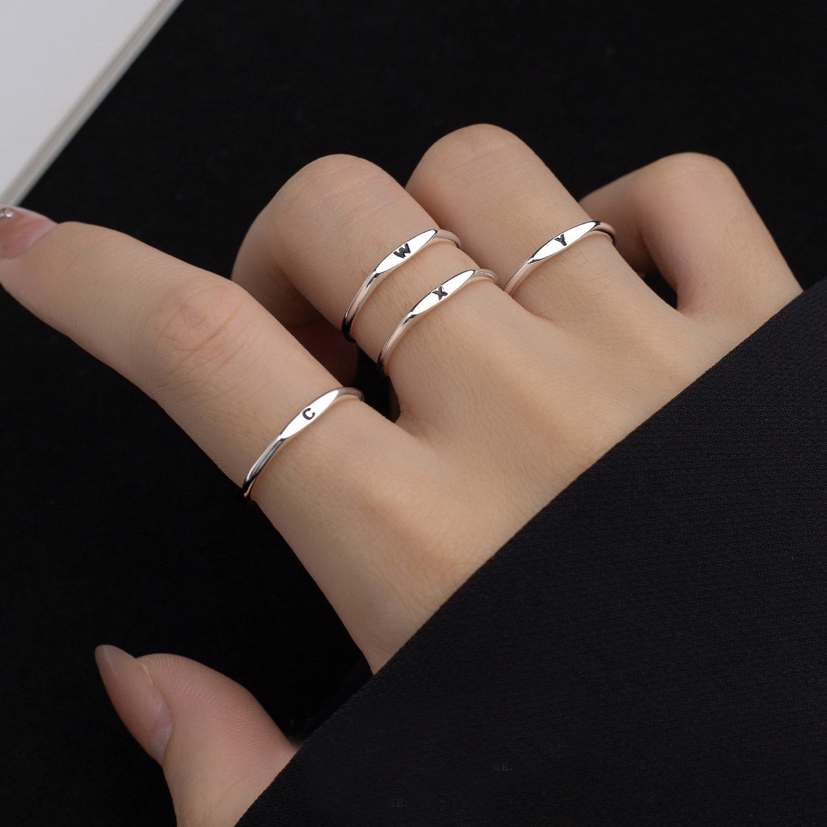 A model wearing multiple 925 sterling silver alphabet rings to create a stacked look.