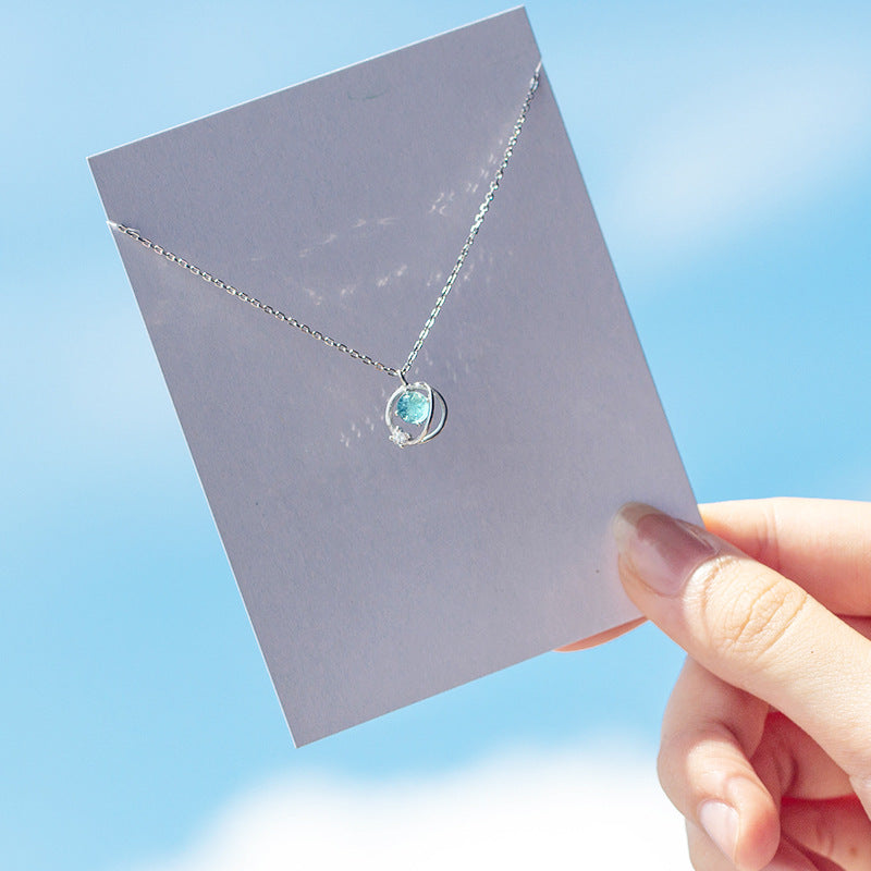 A hand holding the 925 sterling silver planet necklace against a clear sky.