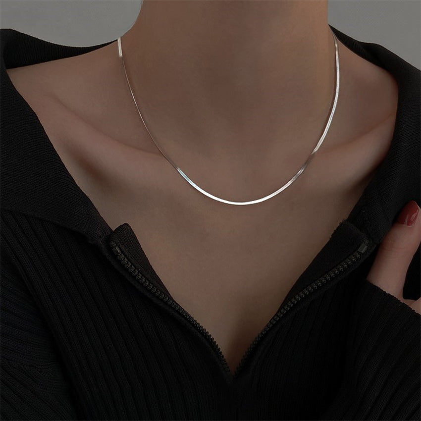 A woman wearing the silver herringbone snake chain necklace with a black top.