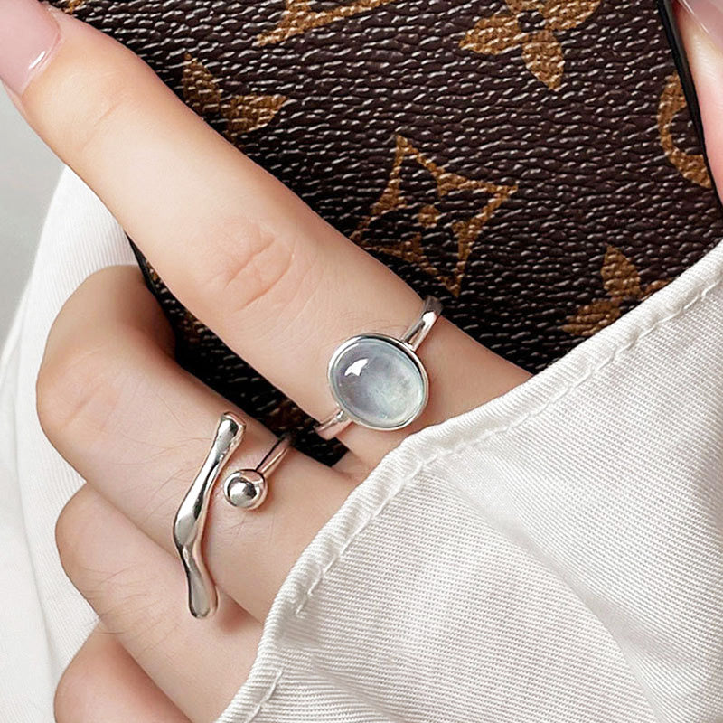 A model's hand showcasing two sterling silver rings from the collection, one with a large white stone and another with a wavy band.