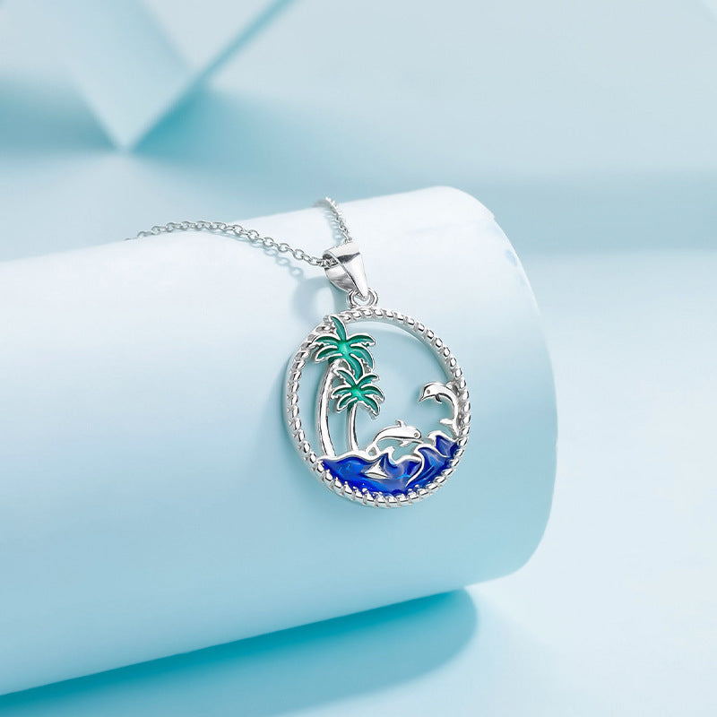 A sterling silver pendant showcasing a beach scene with a palm tree and waves.