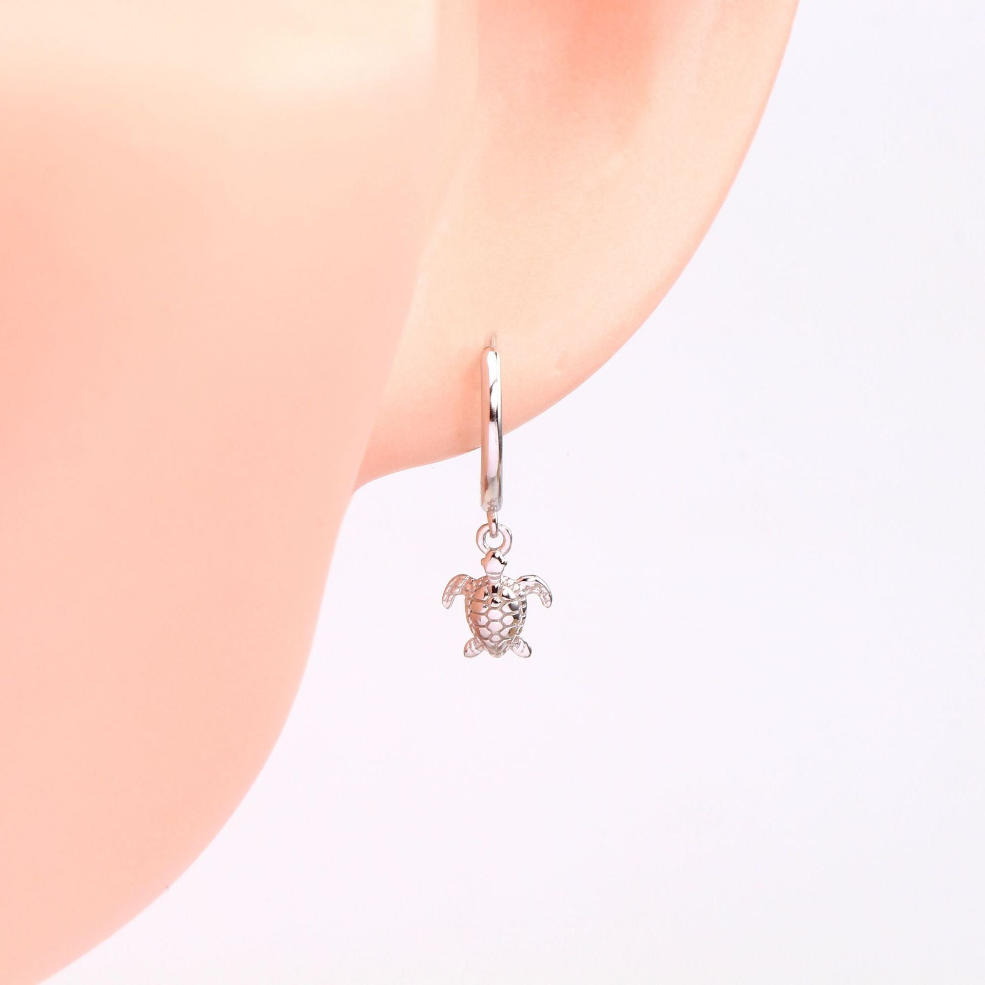 A close-up of the 925 sterling silver turtle earring worn on an ear