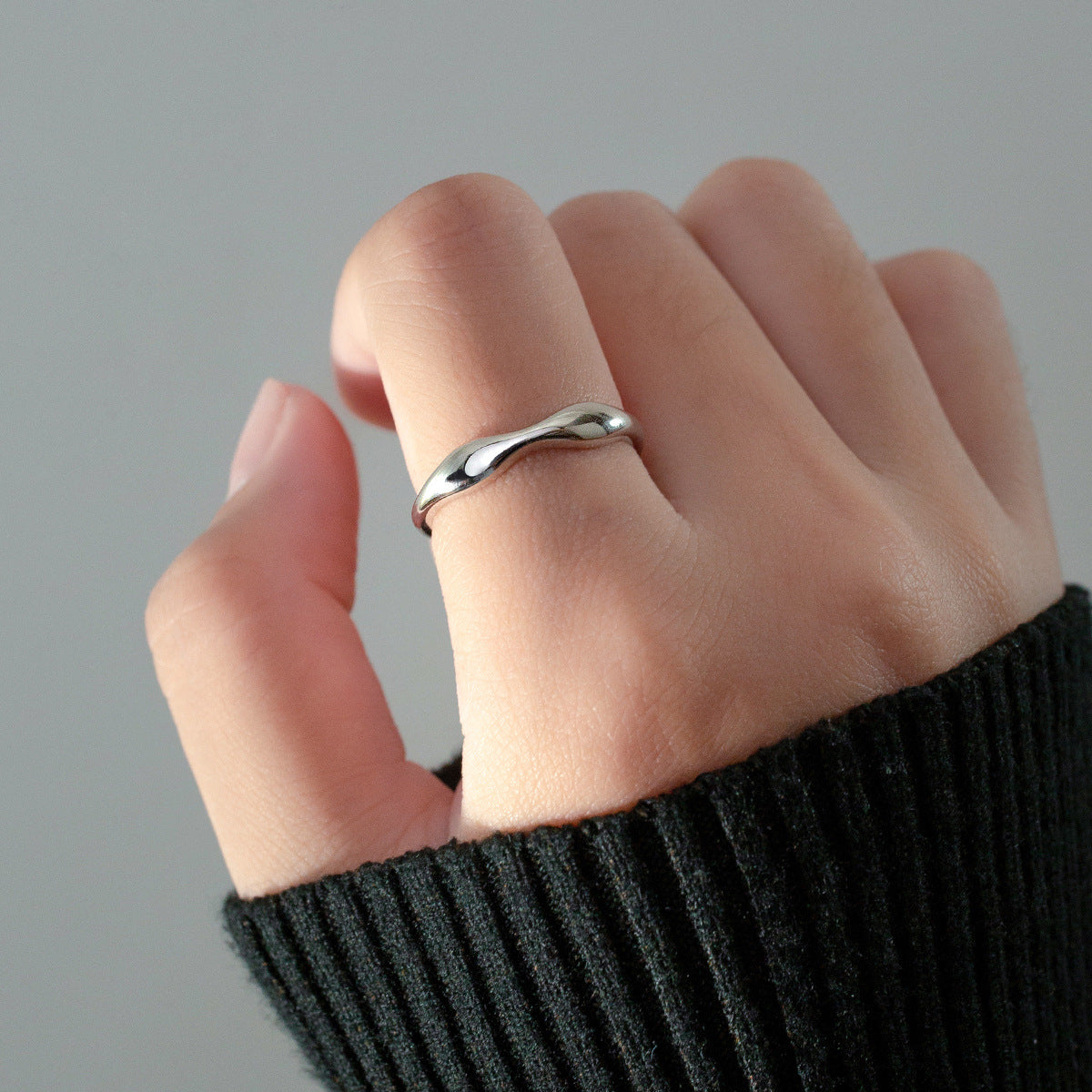 A model's hand adorned with multiple slim wavy sterling silver rings, demonstrating the stackable style.