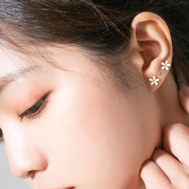 A woman wearing the cute mini enamel daisy flower stud earrings to show their scale and style.