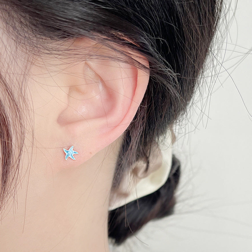 A model wearing the tiny blue enamel starfish stud earring.