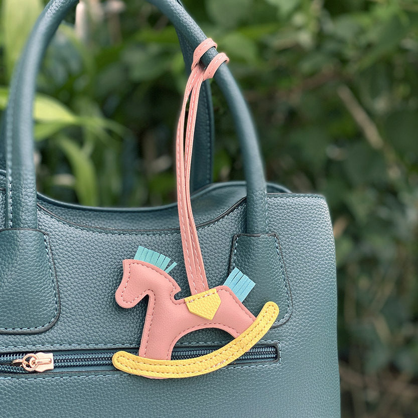 A close-up of the PU leather rocking horse keychain on a teal handbag, showing its texture and braided rope.