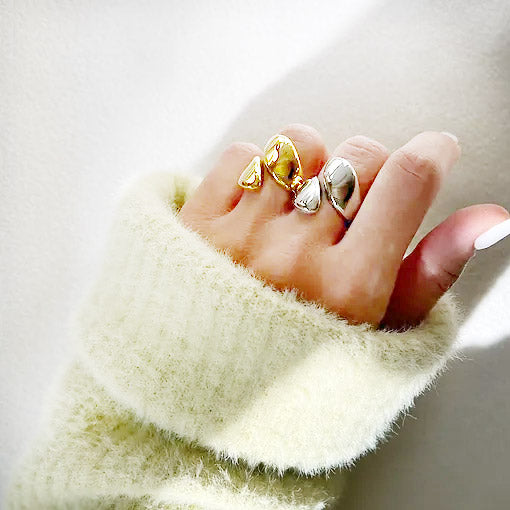 Model wearing teardrop-shaped stainless steel rings in silver and gold.