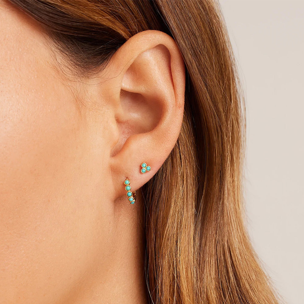 A model wearing two sterling silver turquoise huggie hoop earrings to showcase the style.