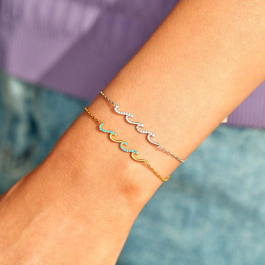 A model's wrist adorned with elegant gold and silver wavy link bracelets from the ocean theme collection.