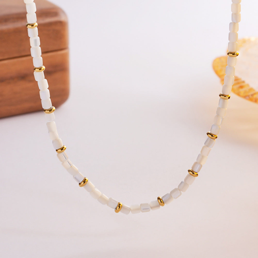 A close-up of the white shell beads and gold accents on the stainless steel necklace