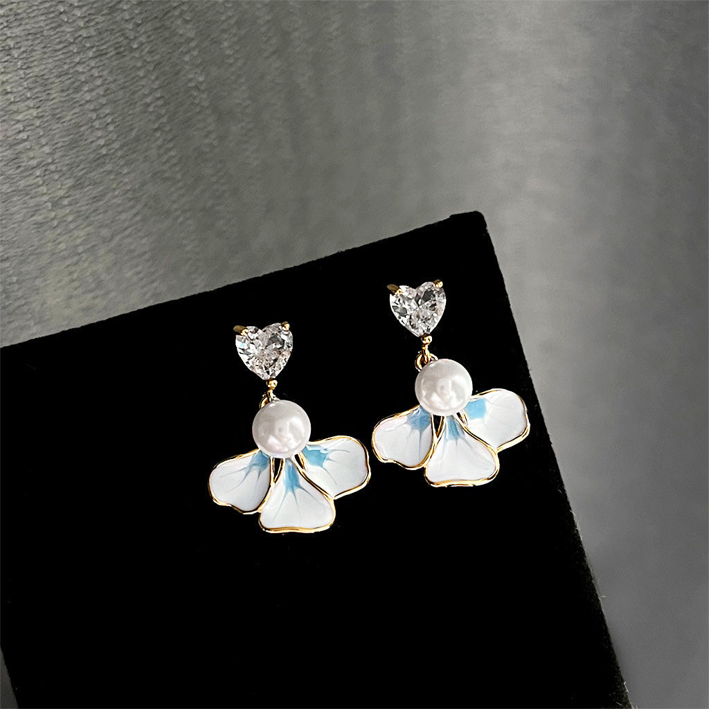 Detailed view of the white and blue enamel flower earrings with gold details