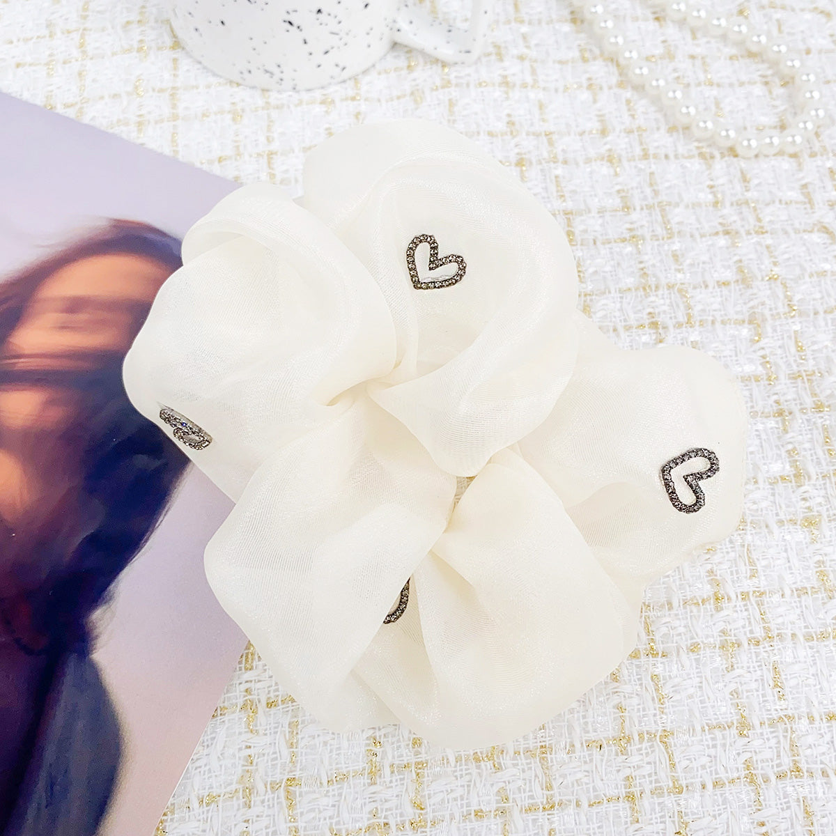 A white silk scrunchie with a delicate heart charm, showcasing its soft texture.