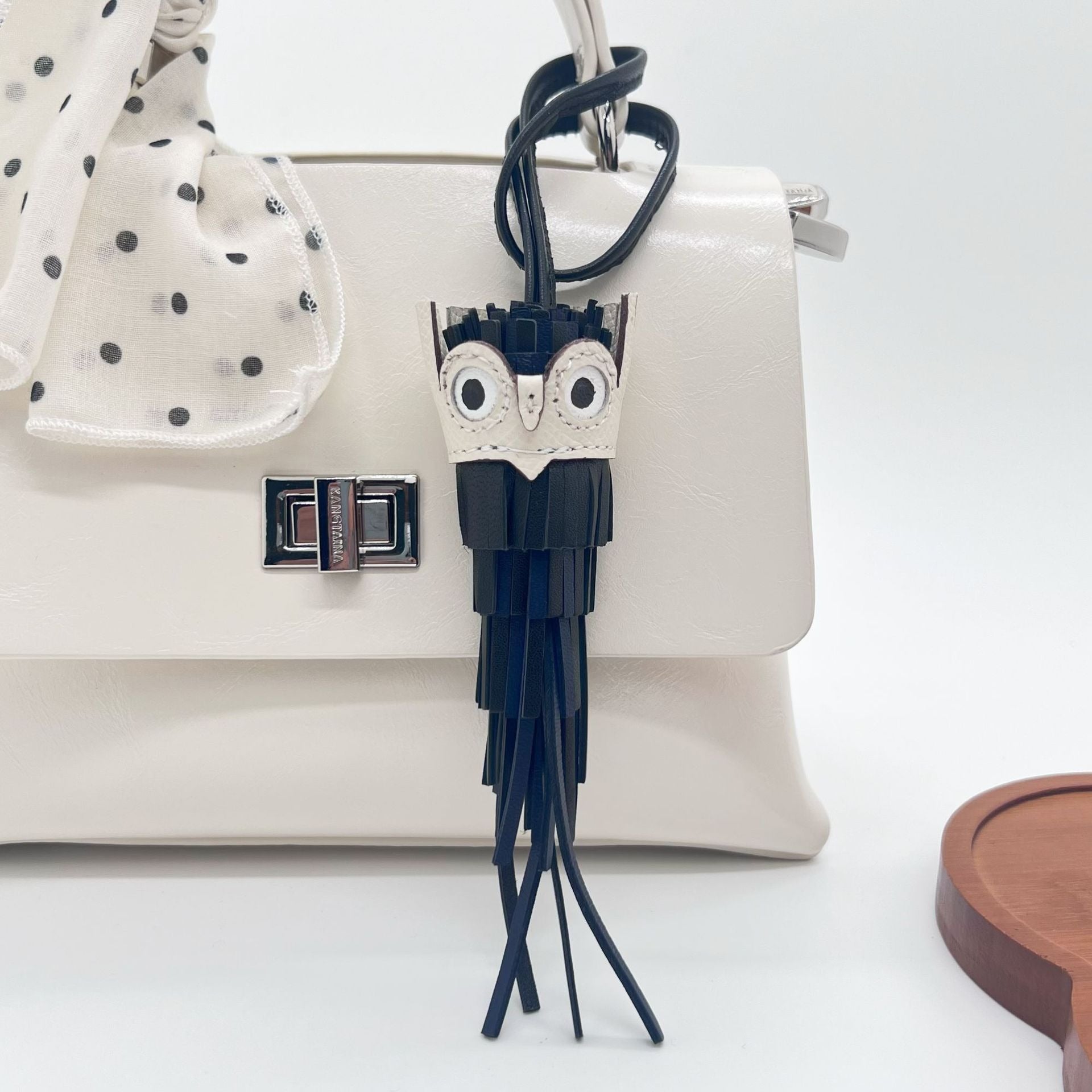 Black leather owl keychain shown as a stylish bag charm on a white handbag