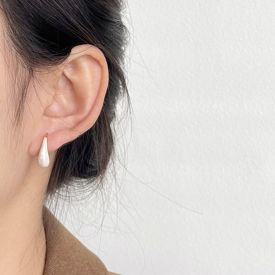A model showcasing the elegant fit of the white teardrop enamel earring.