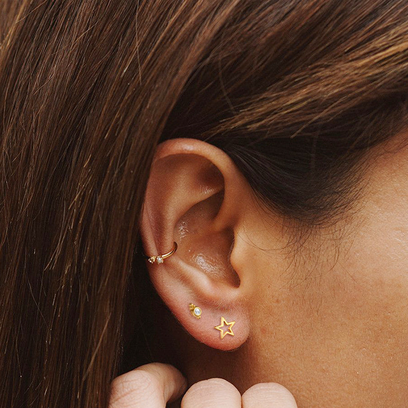 A model's ear adorned with multiple gold earrings, including the hollow star stud.