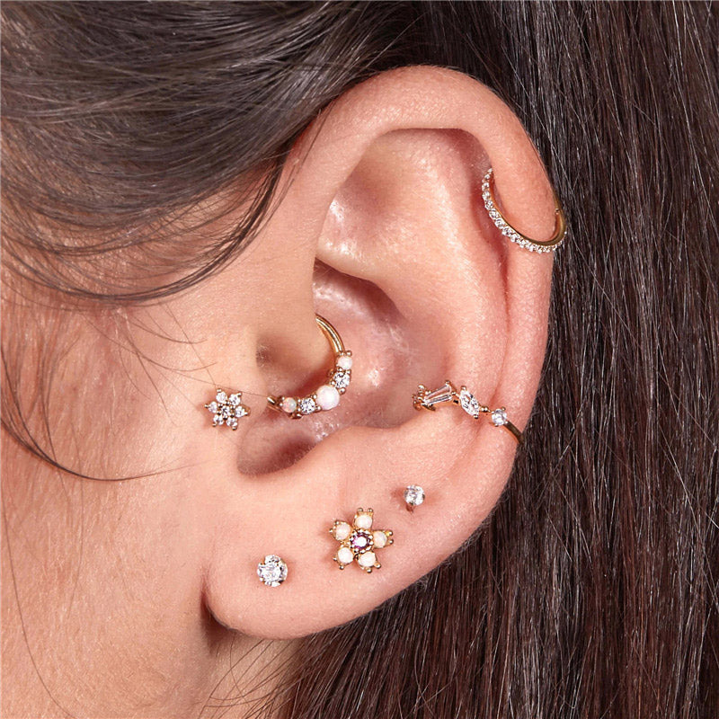 A model's ear adorned with multiple gold earrings, including the tiny opal hoop in a cartilage piercing.