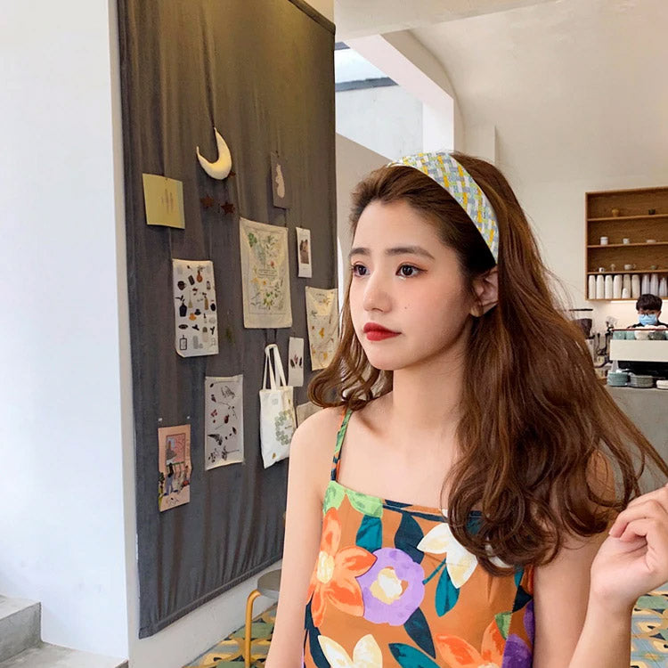 A woman in a cafe wearing a colorful floral outfit and a matching woven headband.