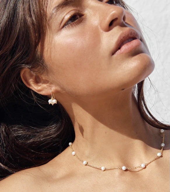 A woman elegantly wearing the gold plated pearl charm necklace and matching earrings.