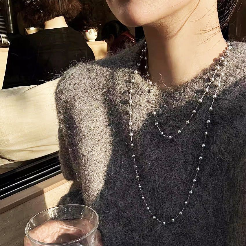 Una mujer con un suéter gris que lleva elegantemente el collar de perlas sintéticas de doble capa.