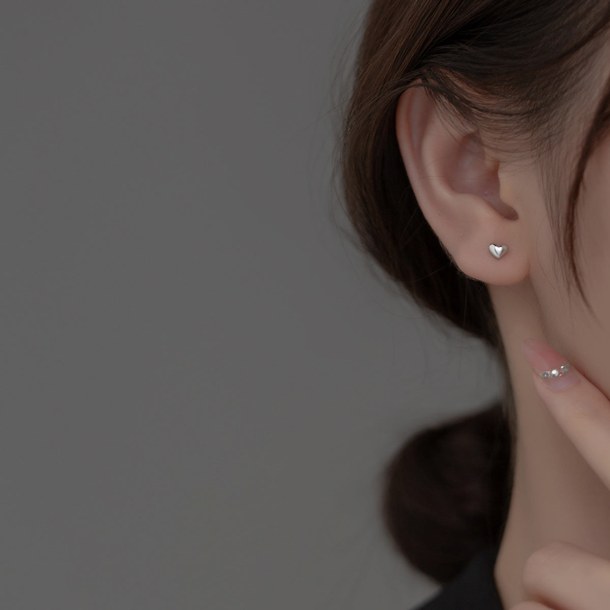 A woman wearing a delicate silver heart stud earring for a subtle look.