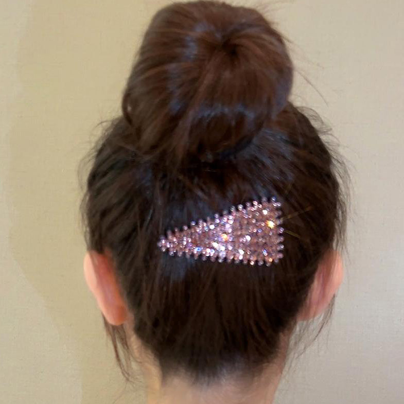 A woman with a stylish bun hairstyle accented with a pink rhinestone triangle hair clip.