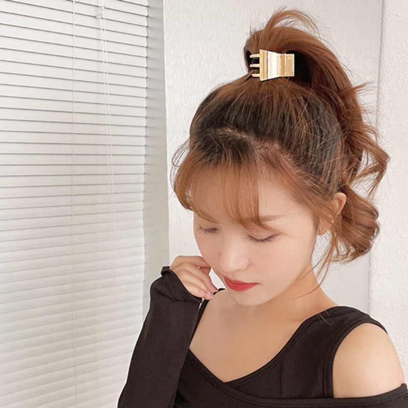 A woman with dark hair wearing a gold metal ponytail clip with a black top.